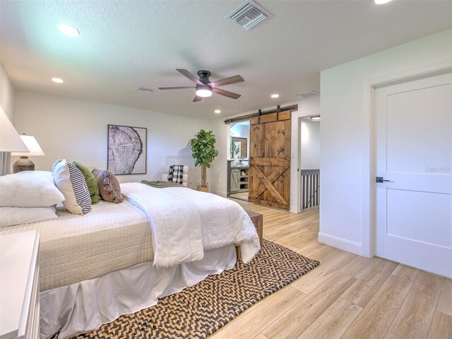 bedroom with a barn door, ceiling fan, light wood-type flooring, and a textured ceiling