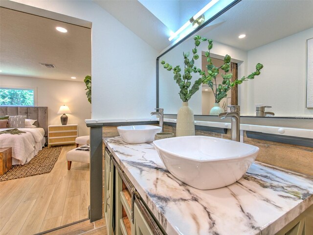 ensuite bathroom featuring ensuite bath, visible vents, wood finished floors, and a sink