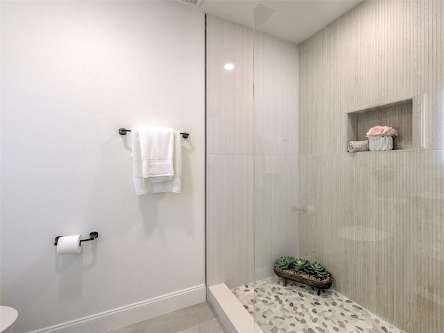 bathroom featuring tiled shower, tile patterned flooring, and toilet