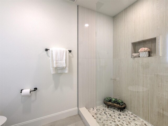 bathroom featuring toilet, baseboards, and tiled shower