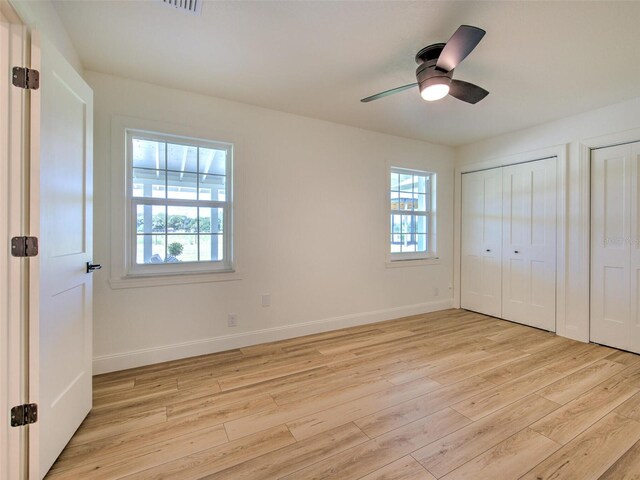 unfurnished bedroom featuring multiple windows, light wood-type flooring, multiple closets, and baseboards