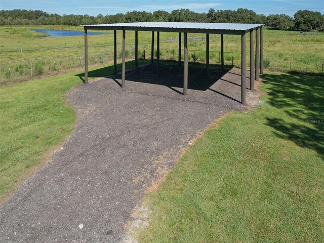 exterior space with driveway, a water view, a detached carport, and fence