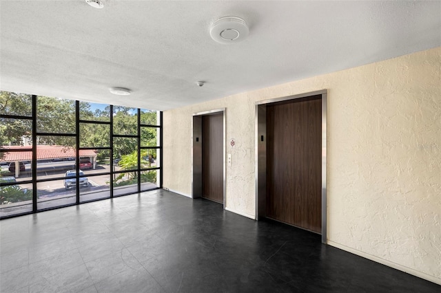 spare room with elevator, a textured ceiling, and a wall of windows