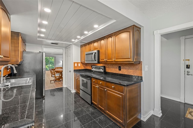 kitchen with backsplash, sink, dark stone countertops, a textured ceiling, and stainless steel appliances