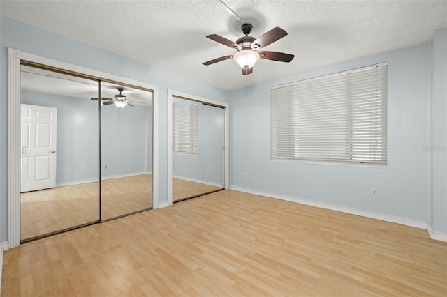 unfurnished bedroom featuring ceiling fan, light hardwood / wood-style floors, a textured ceiling, and two closets