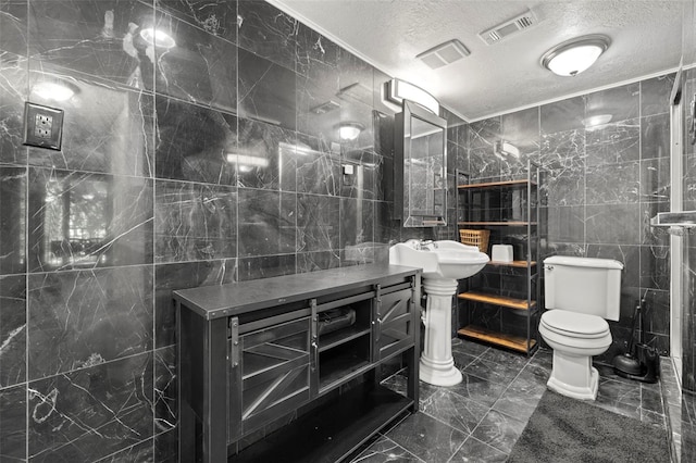 bathroom featuring a textured ceiling, toilet, tile walls, and sink