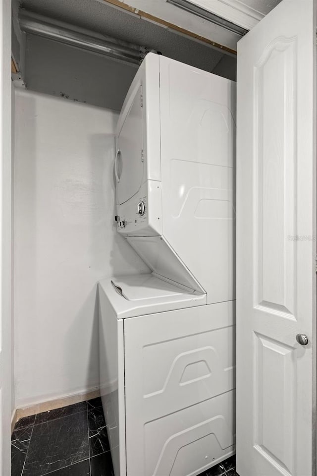 laundry area featuring stacked washer and dryer and dark tile patterned flooring