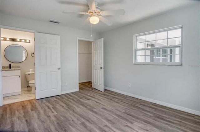 unfurnished bedroom with hardwood / wood-style floors, ceiling fan, ensuite bathroom, and a closet