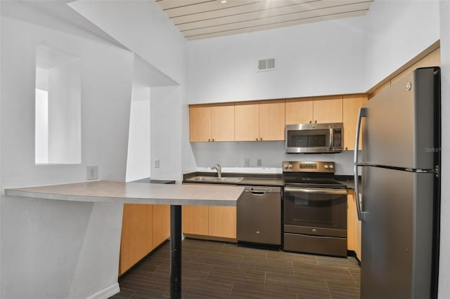 kitchen with appliances with stainless steel finishes, kitchen peninsula, sink, light brown cabinets, and a high ceiling