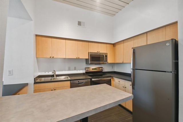 kitchen with appliances with stainless steel finishes, dark tile patterned floors, light brown cabinetry, and sink