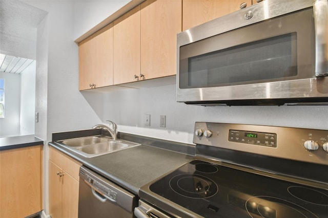 kitchen with stainless steel appliances, dark countertops, light brown cabinets, and a sink