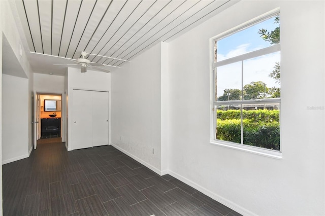 empty room featuring wooden ceiling, plenty of natural light, baseboards, and dark wood finished floors