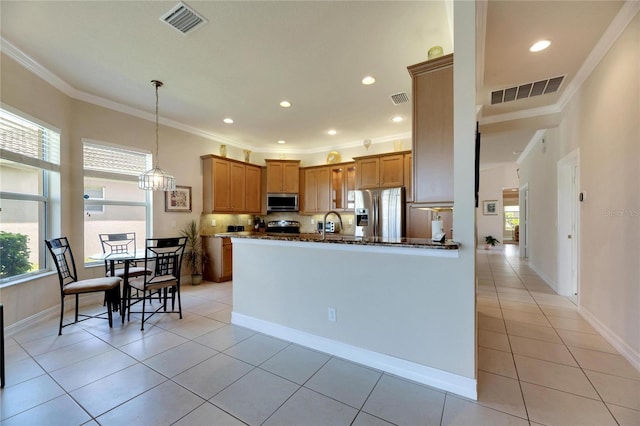 kitchen with dark stone counters, crown molding, hanging light fixtures, light tile patterned floors, and appliances with stainless steel finishes