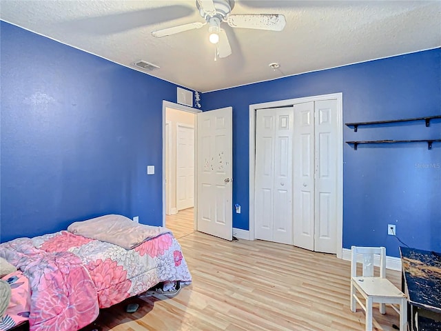 bedroom with a textured ceiling, a closet, light hardwood / wood-style flooring, and ceiling fan