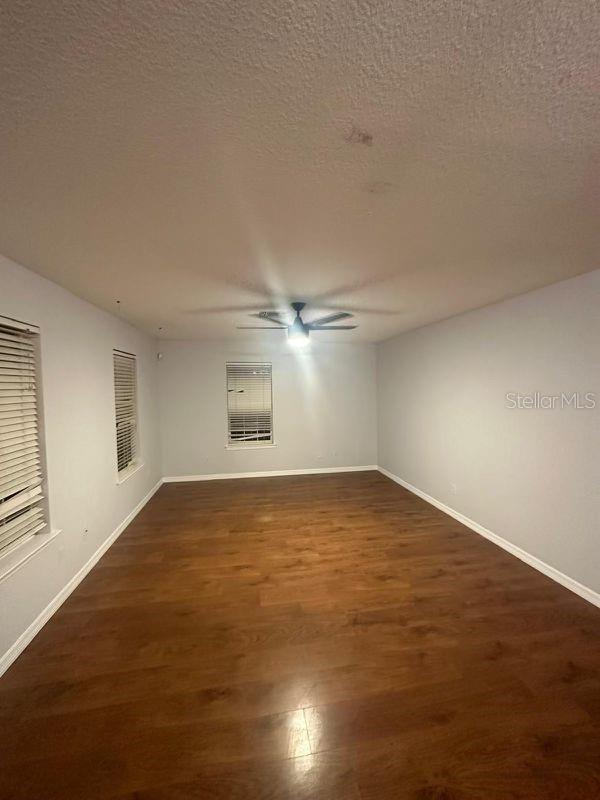 empty room featuring ceiling fan, a textured ceiling, and dark wood-type flooring