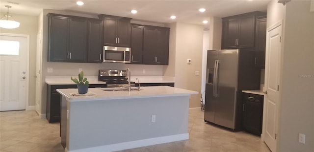 kitchen with appliances with stainless steel finishes, an island with sink, light tile patterned flooring, and pendant lighting