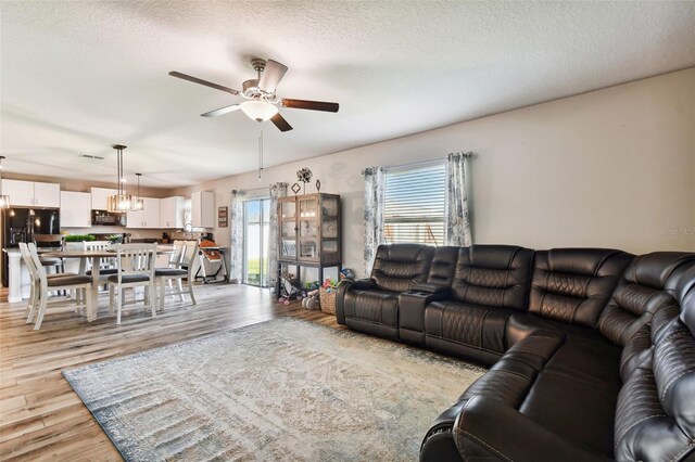 living room featuring ceiling fan with notable chandelier, a textured ceiling, light hardwood / wood-style flooring, and a wealth of natural light