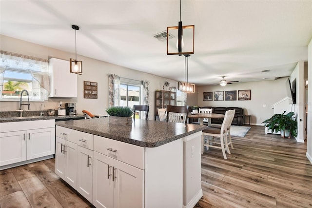 kitchen with dark wood-type flooring, white cabinets, a center island, and sink