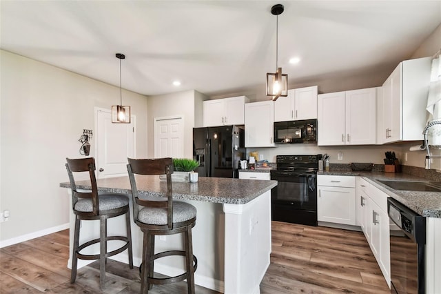 kitchen featuring white cabinets, black appliances, wood-type flooring, pendant lighting, and a kitchen island