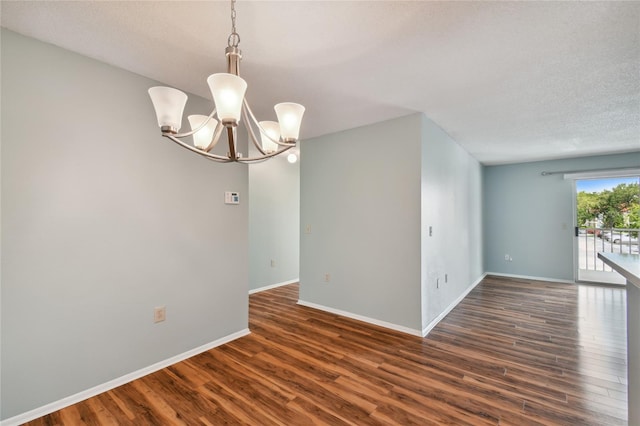 unfurnished room with an inviting chandelier, baseboards, and dark wood finished floors