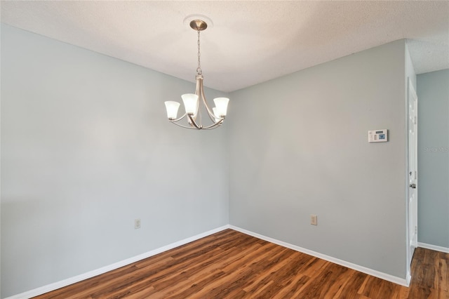 spare room with baseboards, dark wood finished floors, a textured ceiling, and a chandelier