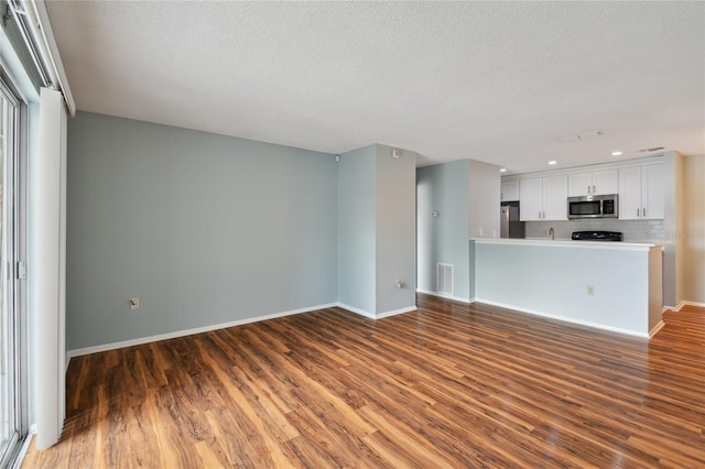 unfurnished living room with a textured ceiling, recessed lighting, wood finished floors, visible vents, and baseboards