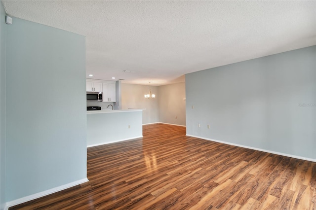 unfurnished living room featuring dark wood-style flooring, a textured ceiling, baseboards, and an inviting chandelier