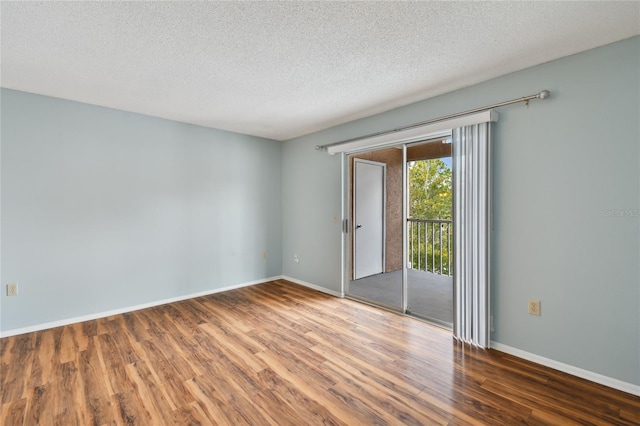 empty room with a textured ceiling, wood finished floors, and baseboards