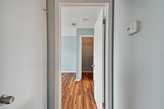 hall with baseboards, visible vents, a textured ceiling, and wood finished floors