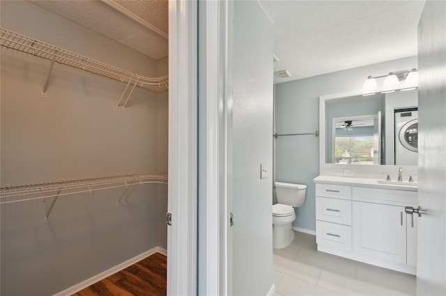 full bath with a textured ceiling, toilet, vanity, baseboards, and stacked washer / drying machine