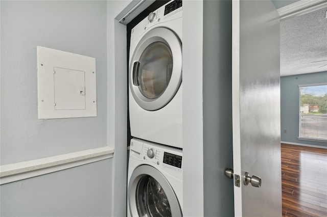 laundry room with a textured ceiling, laundry area, wood finished floors, electric panel, and stacked washer and clothes dryer