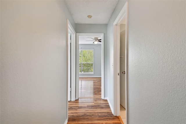 hall with a textured wall, a textured ceiling, baseboards, and wood finished floors