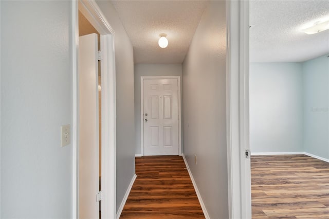 hallway with a textured ceiling, baseboards, and wood finished floors