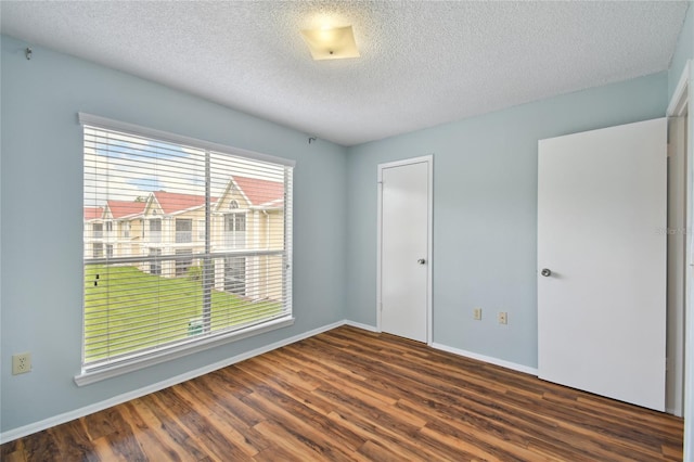 empty room with a textured ceiling, wood finished floors, and baseboards