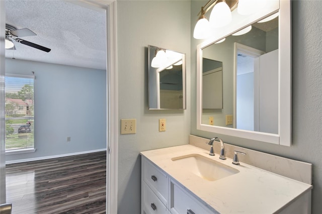 bathroom with a ceiling fan, a textured ceiling, vanity, wood finished floors, and baseboards