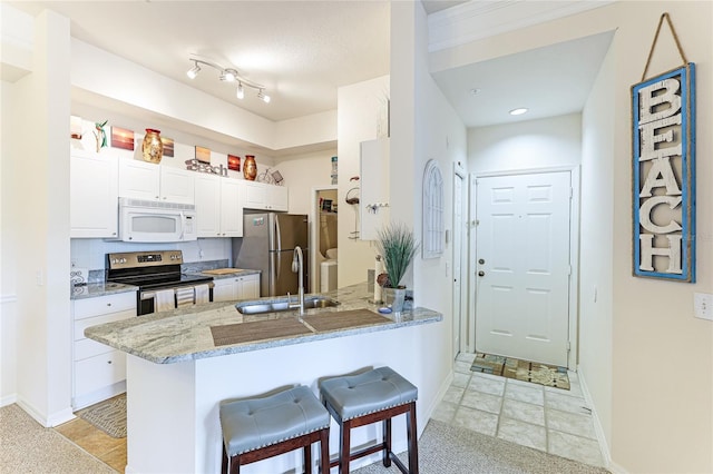 kitchen featuring stainless steel appliances, white cabinets, a sink, light stone countertops, and a peninsula