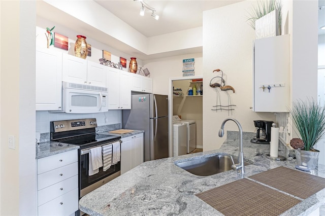 kitchen featuring light stone counters, stainless steel appliances, washing machine and dryer, white cabinetry, and a sink