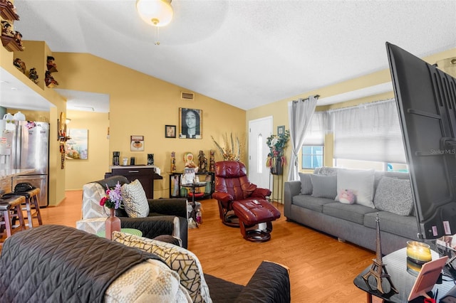 living room featuring light wood-type flooring, ceiling fan, a textured ceiling, and vaulted ceiling