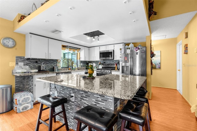 kitchen featuring a center island, light stone countertops, appliances with stainless steel finishes, light hardwood / wood-style floors, and white cabinetry