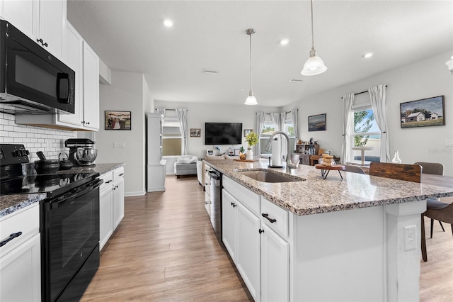 kitchen featuring light wood finished floors, a sink, backsplash, and black appliances