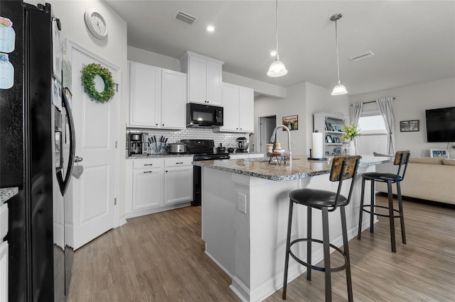 kitchen with a kitchen breakfast bar, light stone countertops, light wood-style floors, visible vents, and black appliances