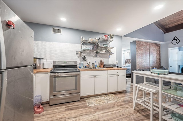 kitchen featuring stainless steel appliances, wooden counters, sink, vaulted ceiling, and light hardwood / wood-style floors