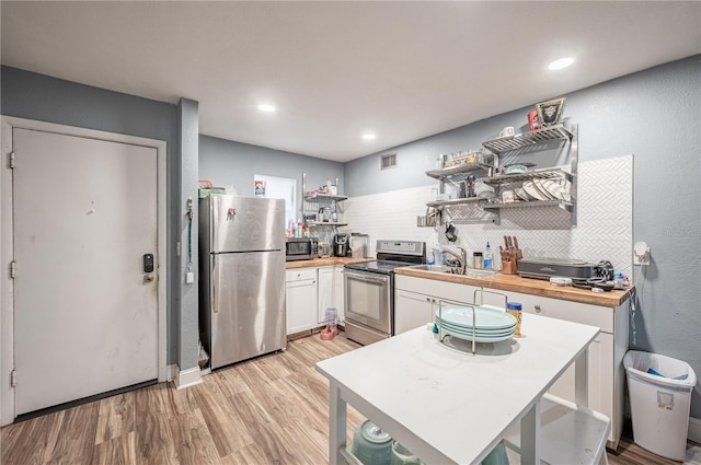 kitchen with wooden counters, open shelves, a sink, stainless steel appliances, and white cabinets