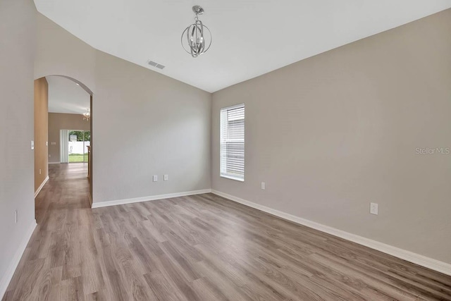 spare room with vaulted ceiling, a chandelier, and light hardwood / wood-style floors