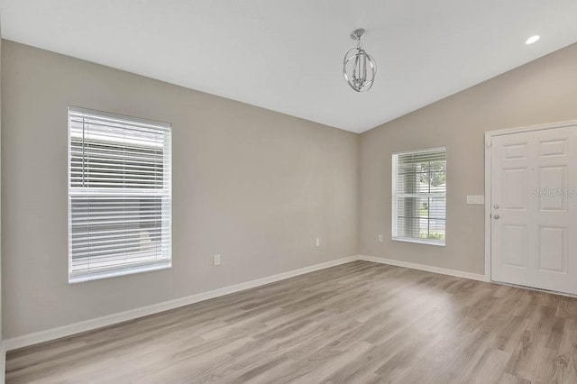 unfurnished room with lofted ceiling, a chandelier, and light hardwood / wood-style flooring