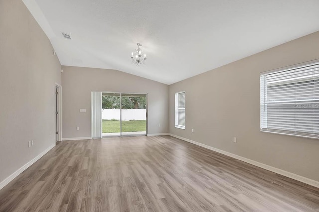 empty room featuring lofted ceiling, hardwood / wood-style flooring, and a chandelier