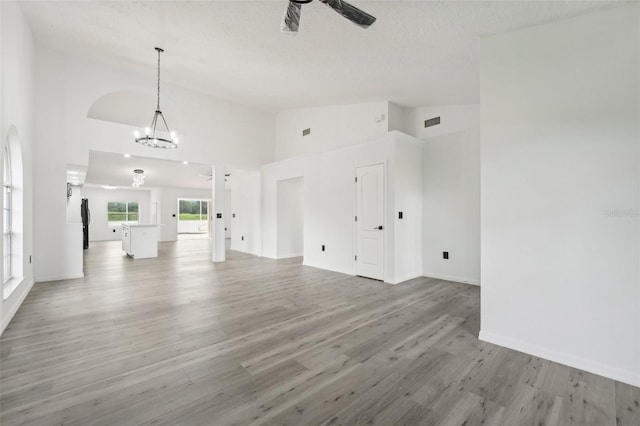 unfurnished living room with ceiling fan with notable chandelier, light hardwood / wood-style flooring, high vaulted ceiling, and a textured ceiling