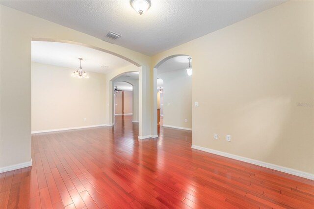 empty room featuring a textured ceiling, a notable chandelier, and hardwood / wood-style flooring