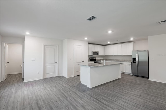 kitchen with a kitchen island with sink, white cabinetry, light hardwood / wood-style flooring, light stone countertops, and appliances with stainless steel finishes