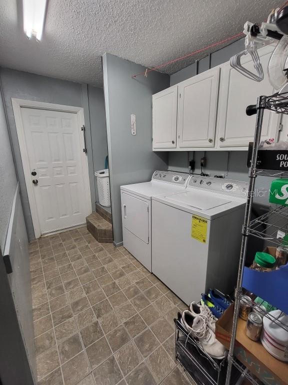 clothes washing area featuring washing machine and dryer, cabinets, and a textured ceiling